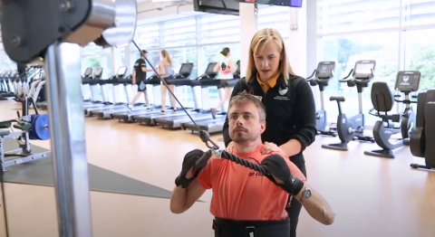 A disabled participation working out in the gym with support from a fitness instructor. 