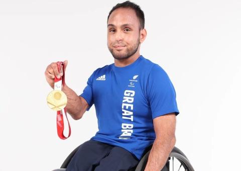 Image of person in wheelchair holding a gold medal, smiling at camera 