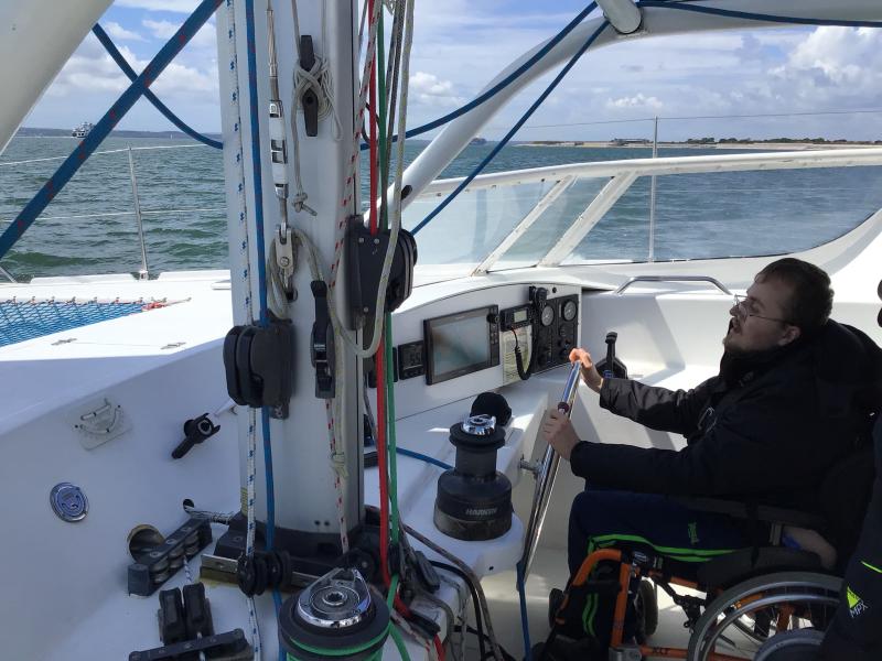 A young male wheelchair user at the helm of a sailing boat