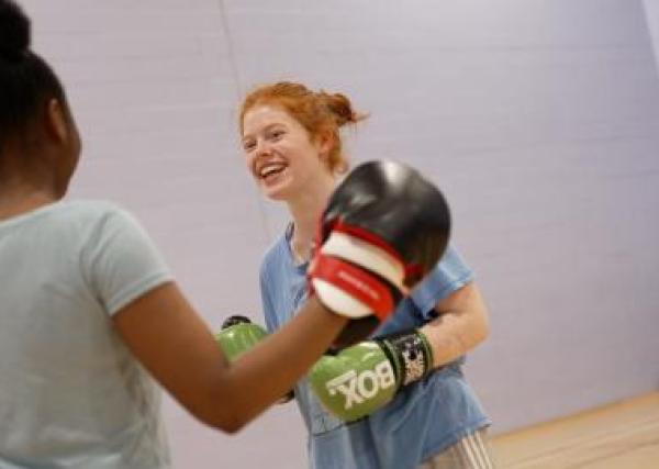 Two females smiling and training boxercise in a sports hall.