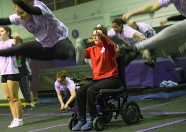 Inclusive cheerleading session in action with female athletes jumping and a wheelchair athlete in the middle.