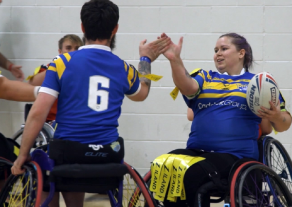 Wheelchair rugby league players high fiving with the ball in hand.