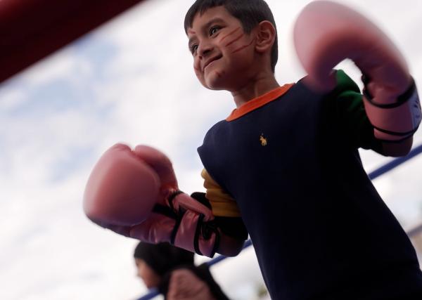 Young adaptive boxer, wearing facepaint and with gloves held high, smiling off camera.